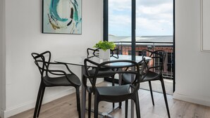 A modern dining area with a glass table and black chairs, a potted plant, and a large abstract painting on the wall. - Greenwich 602 (Cape Town)