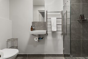 Un baño moderno con lavamanos blanco, cabina de ducha de vidrio y un perchero para toallas.