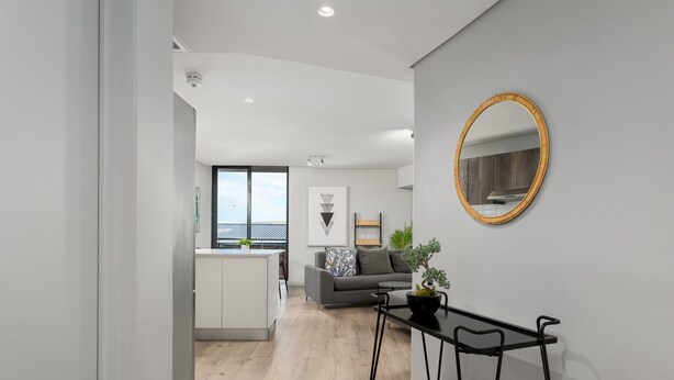 A modern living room with a grey sofa, a small table with a plant, and a round mirror on the wall. - Greenwich 602 (Cape Town)