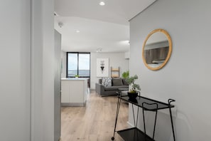Een moderne woonkamer met een grijze bank, een klein tafeltje met een plant en een ronde spiegel aan de muur.