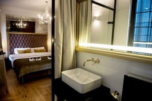 A bedroom with a large bed, a bedside table, a mirror, and a window with curtains.