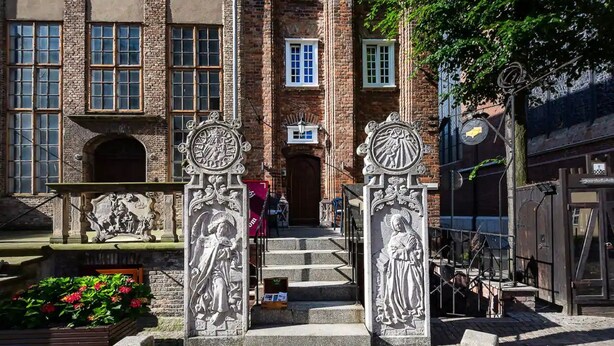 Un edificio histórico con fachada de ladrillo, entrada central con escalones y decorativos grabados de piedra.