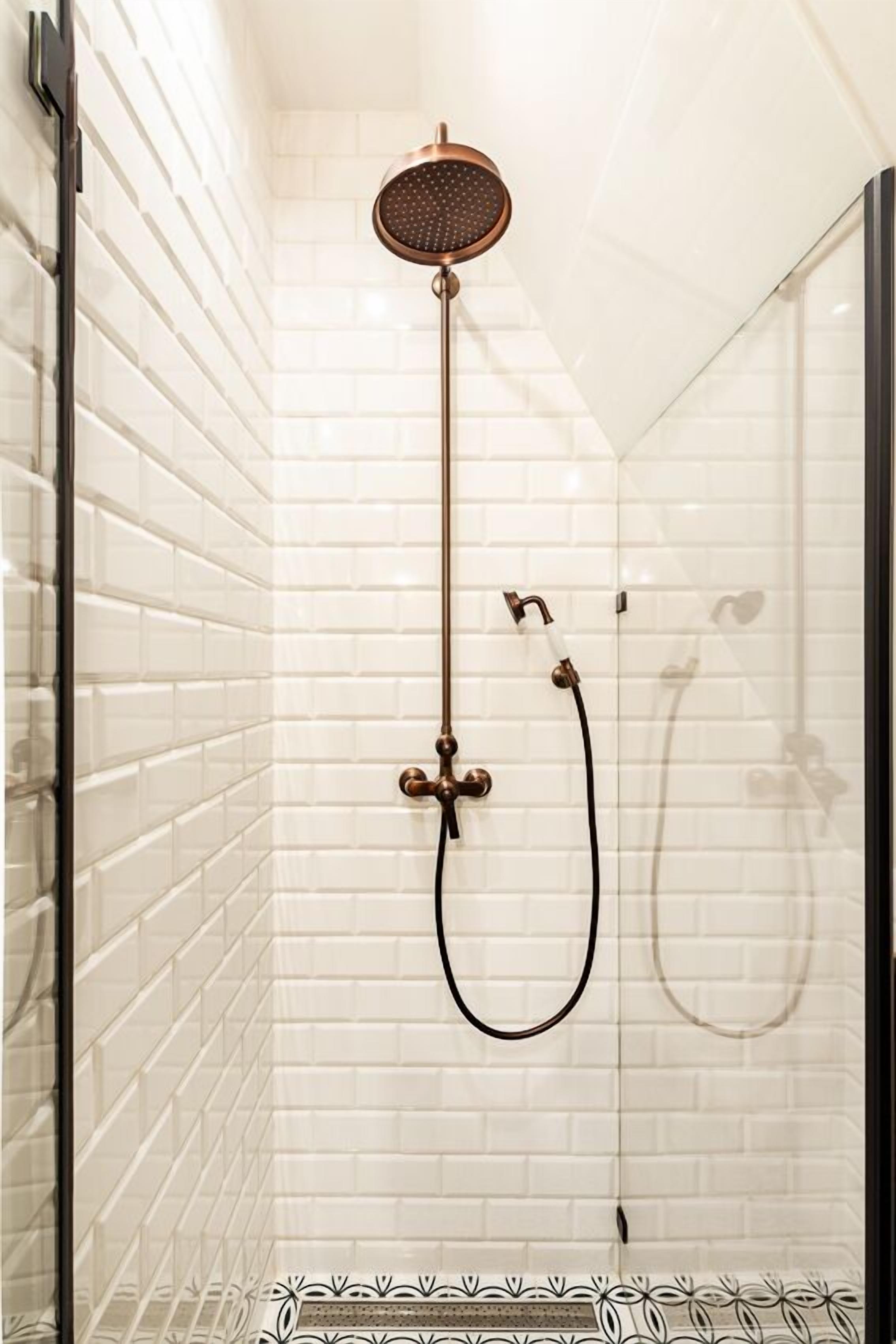 A glass-enclosed shower with white tiled walls and a brass showerhead.