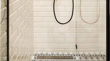A glass-enclosed shower with white tiled walls and a brass showerhead.