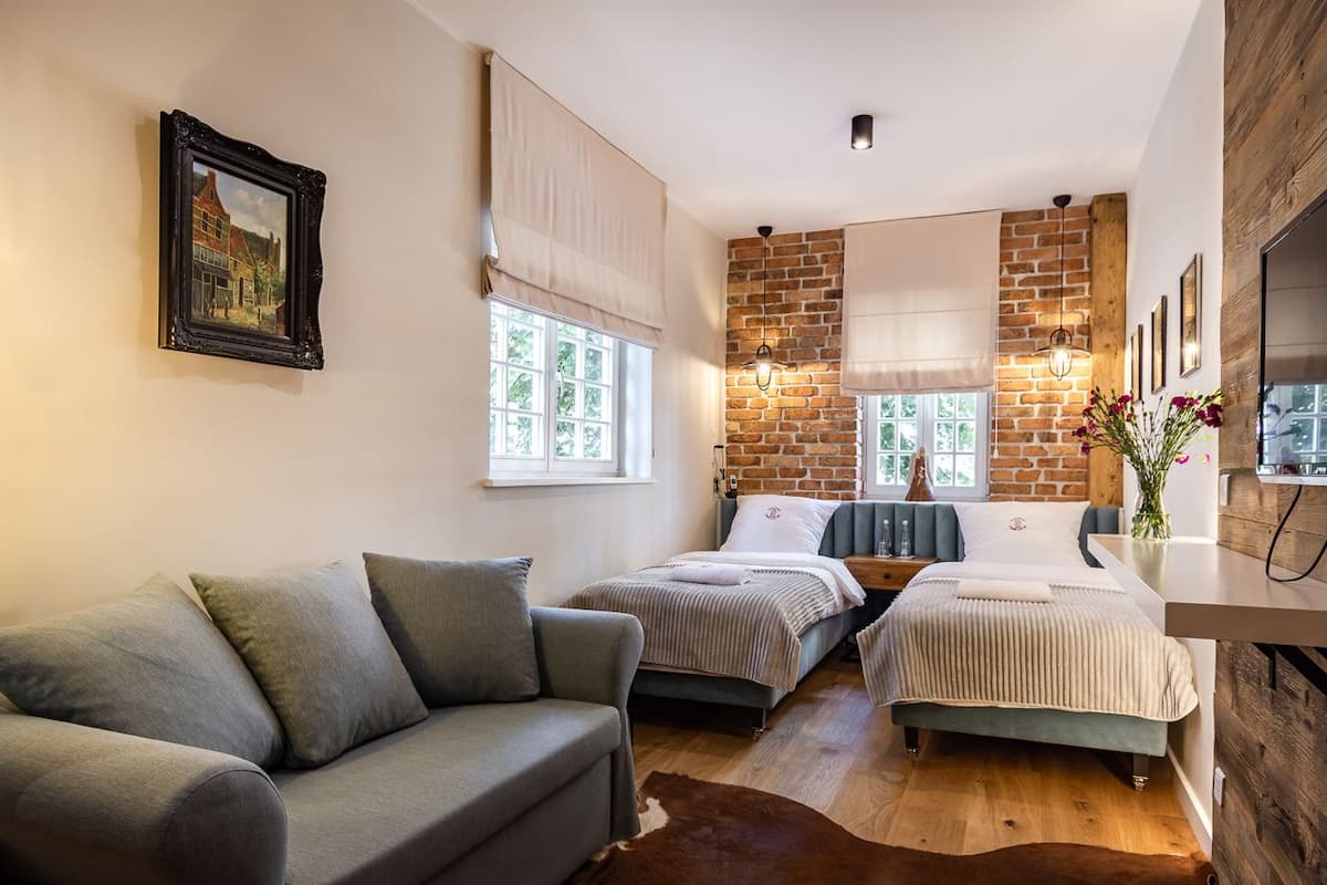 A cozy bedroom with a brick wall, two beds, a sofa, and a wooden desk.