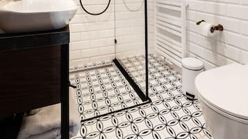 A modern bathroom with a white tiled shower, a sink with a dark countertop, and a toilet with a white lid.