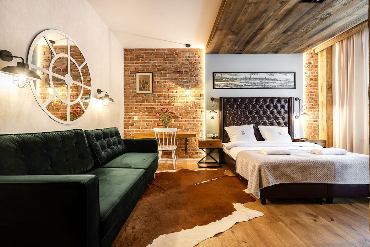 A cozy bedroom with a brick wall, a round mirror, a green sofa, a bed with a headboard, and a cowhide rug.