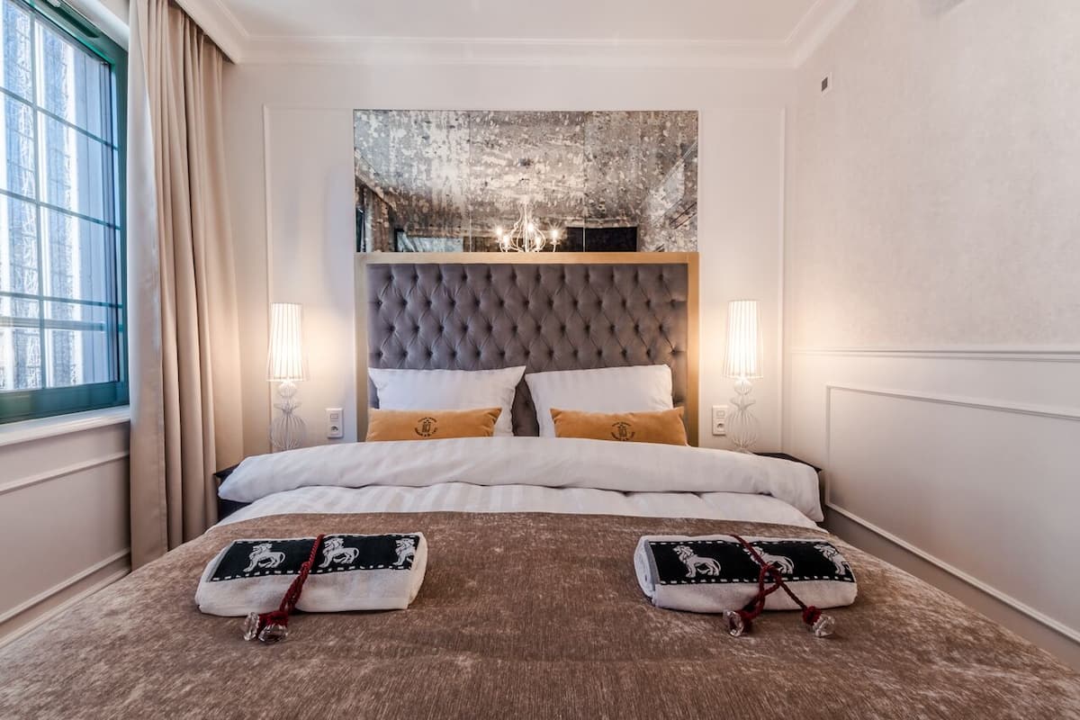 A hotel room with a large bed, a tufted headboard, two bedside lamps, and a large window with curtains.