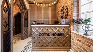Una recepción con el cartel "COTYK HOUSE", una araña, pared de ladrillo y una ventana con flores.