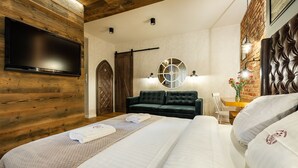 Una habitación de hotel moderna con una cama grande, un televisor de pantalla plana montado en una pared de madera, un sofá de color oscuro y una pared de ladrillo decorativa.
