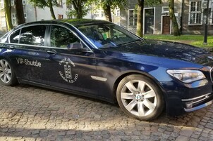 A dark blue car with "VIP-Shuttle" and "Gdansk N.D. 151" on the side parked on a cobblestone street.