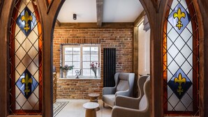 Una habitación con pared de ladrillo, ventana con vistas y zona de estar con una silla y una mesita.