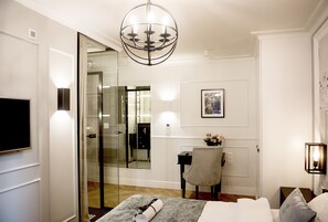 Camera d'albergo con un letto, una scrivania con una sedia, una televisione, un lampadario e uno specchio.
