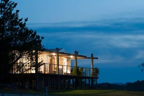 Une maison avec un porche et une cour clôturée, au crépuscule.