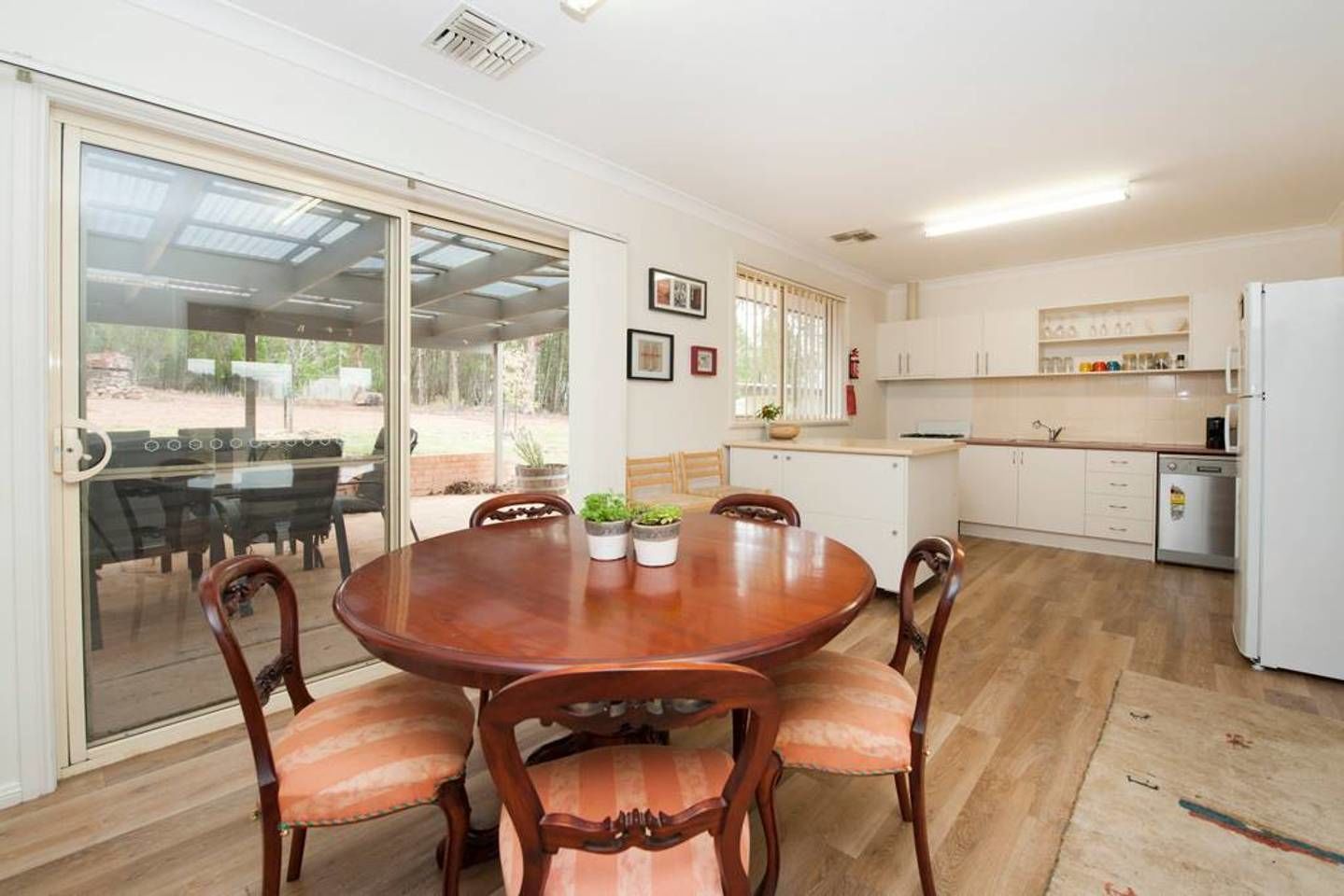 A dining area with a round wooden table and chairs, a kitchen with white cabinets, and a sliding glass door leading to an outdoor area.