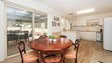 A dining area with a round wooden table and chairs, a kitchen with white cabinets, and a sliding glass door leading to an outdoor area.