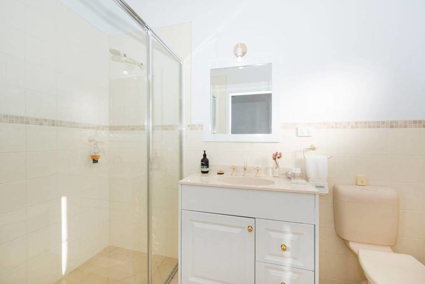Un baño con cabina de ducha de vidrio, un lavamanos blanco con espejo y un inodoro.