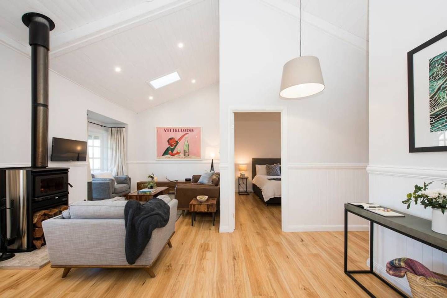 A modern living room with a fireplace, a sofa, a coffee table, and a bed in the adjacent room.