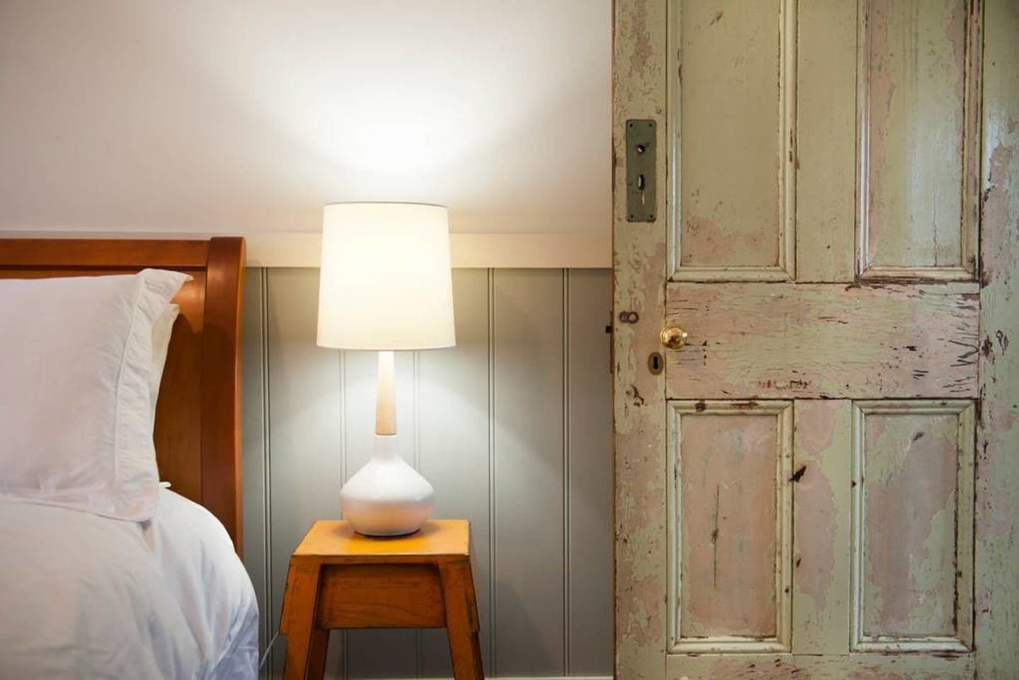 A room with a bed, a bedside table with a lamp, and a wooden door.