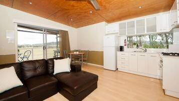 Una sala de estar moderna con un sofá de cuero marrón, un comedor con mesa y sillas, y una cocina con armarios blancos y estufa.