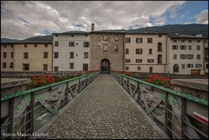 A cobblestone bridge leading to a historic building with multiple windows and a central archway. - Le Stanze del Trenino Rosso (Tirano)
