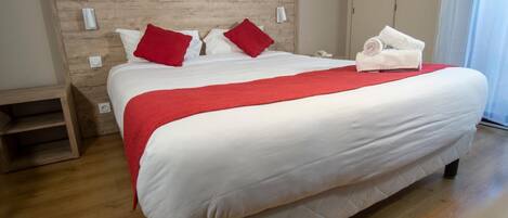 A neatly made bed with white and red bedding, a wooden headboard, and a red throw blanket.