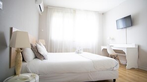 A hotel room with a bed, a desk, a chair, a television, and a window with curtains.