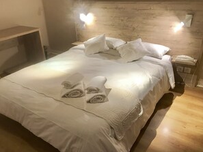 A neatly made bed with white linens and rolled towels, a wooden headboard with wall-mounted lights, and a bedside telephone. - Hôtel Pyrène (Foix)