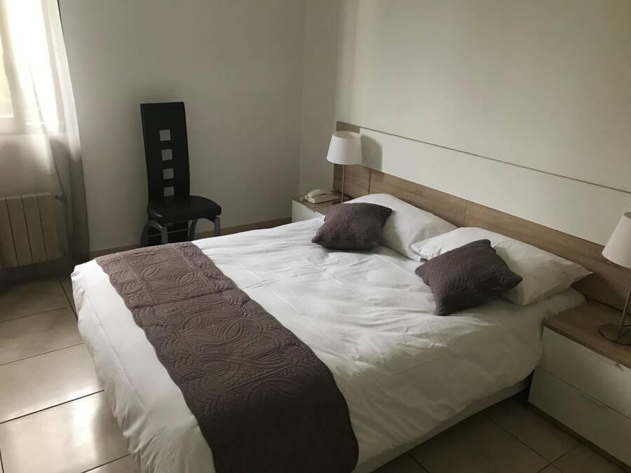 Un lit bien fait, agrémenté d’un couvre-lit à motifs, deux lampes de chevet et une chaise dans une chambre d’hôtel.
