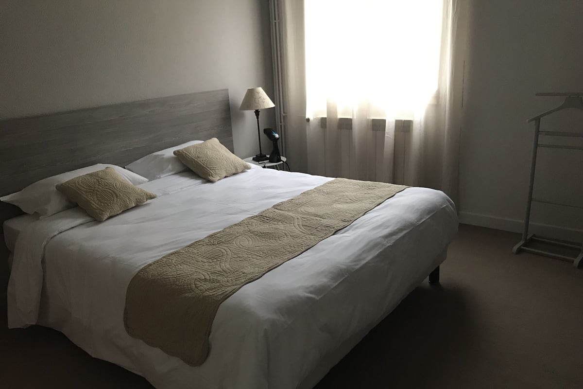Un lit bien fait, avec une tête de lit, deux oreillers et un plaid décoratif.
