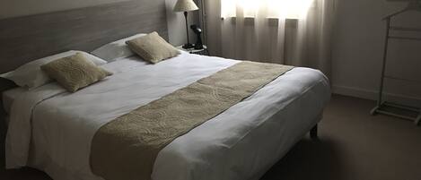 Una cama bien tendida con cabecera, dos almohadas y una manta decorativa.