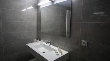 Un baño moderno con un lavamanos blanco, espejo y baldosas grises.