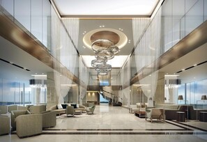 A spacious lobby with a grand chandelier, a staircase, and modern seating arrangements.