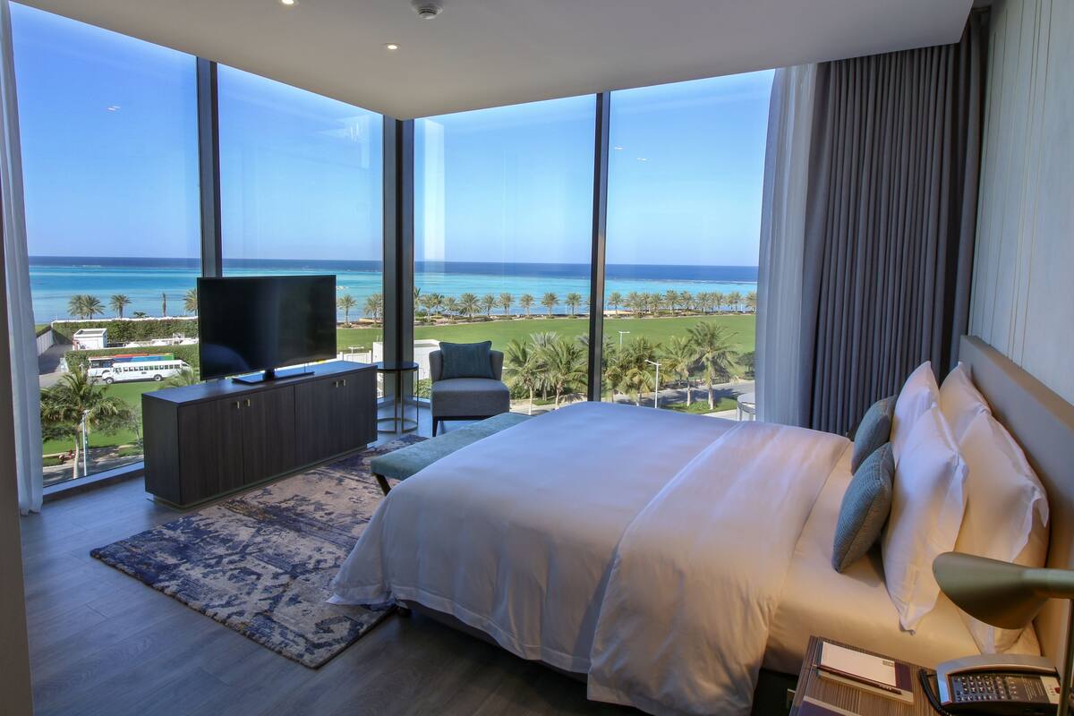 A bedroom with a large bed, a TV, and a view of the ocean.