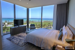 A bedroom with a large bed, a TV, and a view of the ocean.