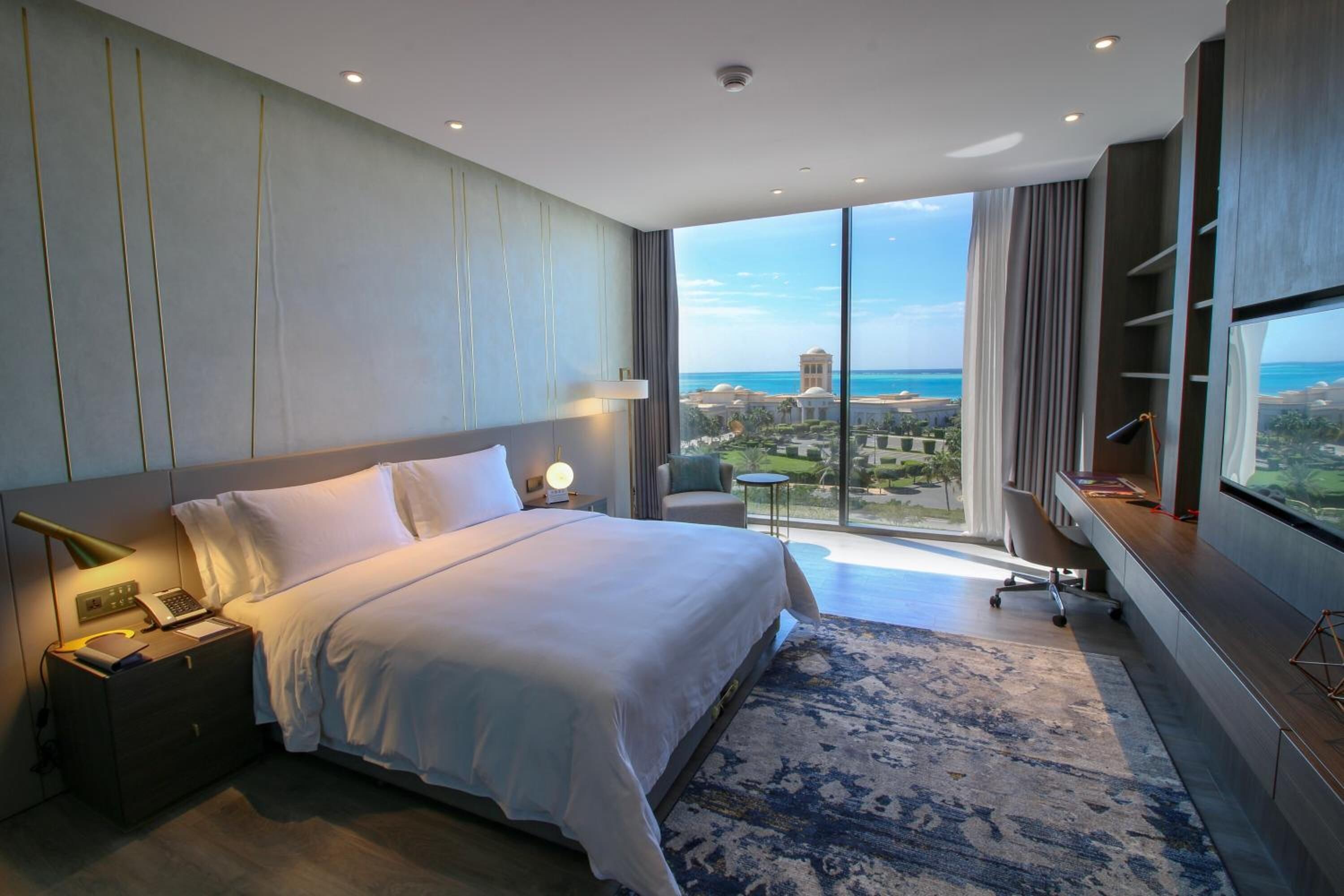 A modern hotel room with a large bed, a desk, and a view of the cityscape.