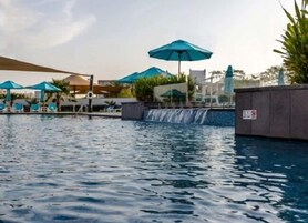 A swimming pool with a waterfall feature, lounge chairs, and umbrellas.