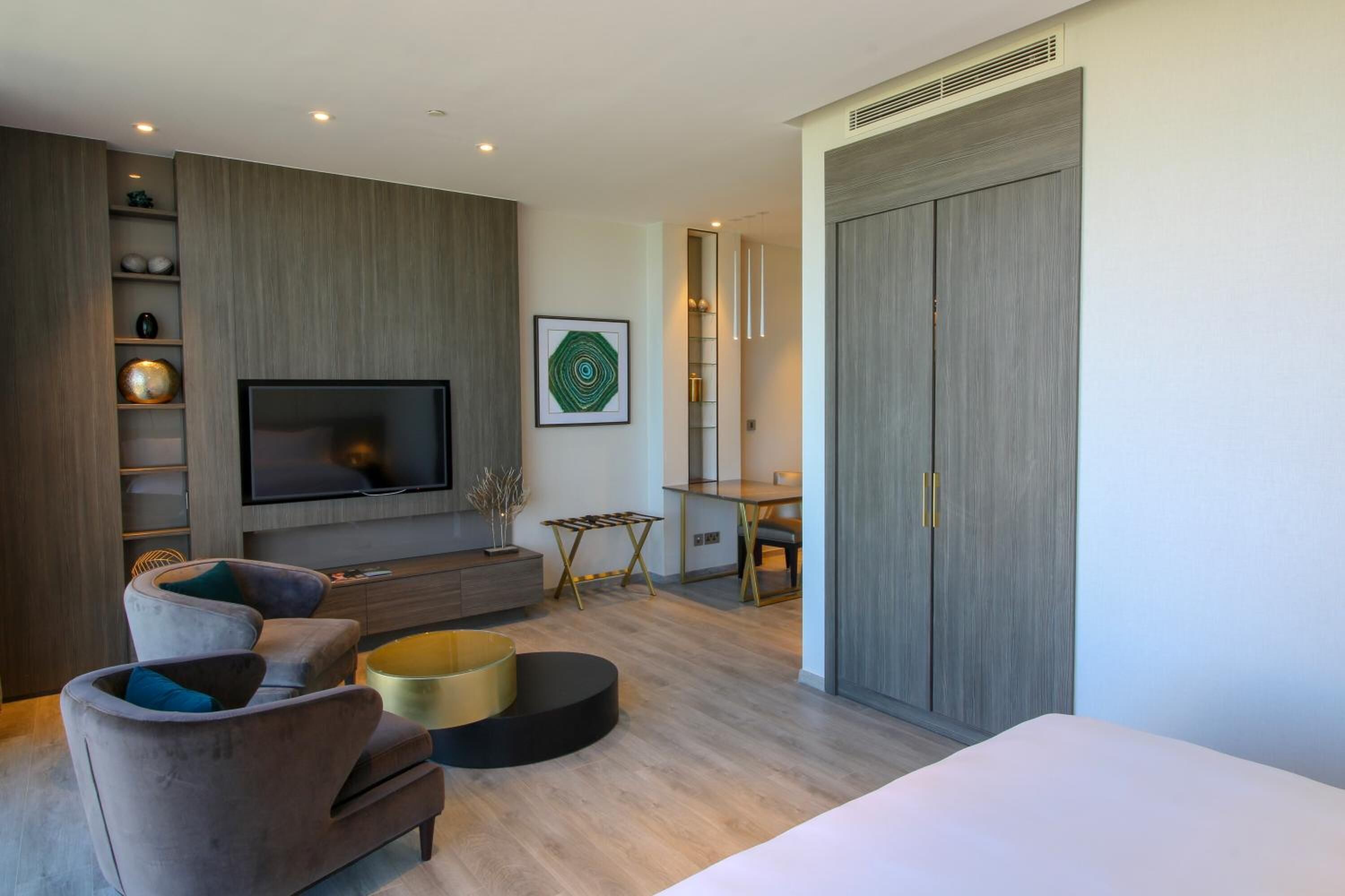 A modern bedroom with a large bed, a TV mounted on the wall, a desk, and a wardrobe.