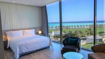 Enjoy a panoramic ocean view from the large window in this stylish room, featuring a comfortable bed and a seating area with a sofa and table.