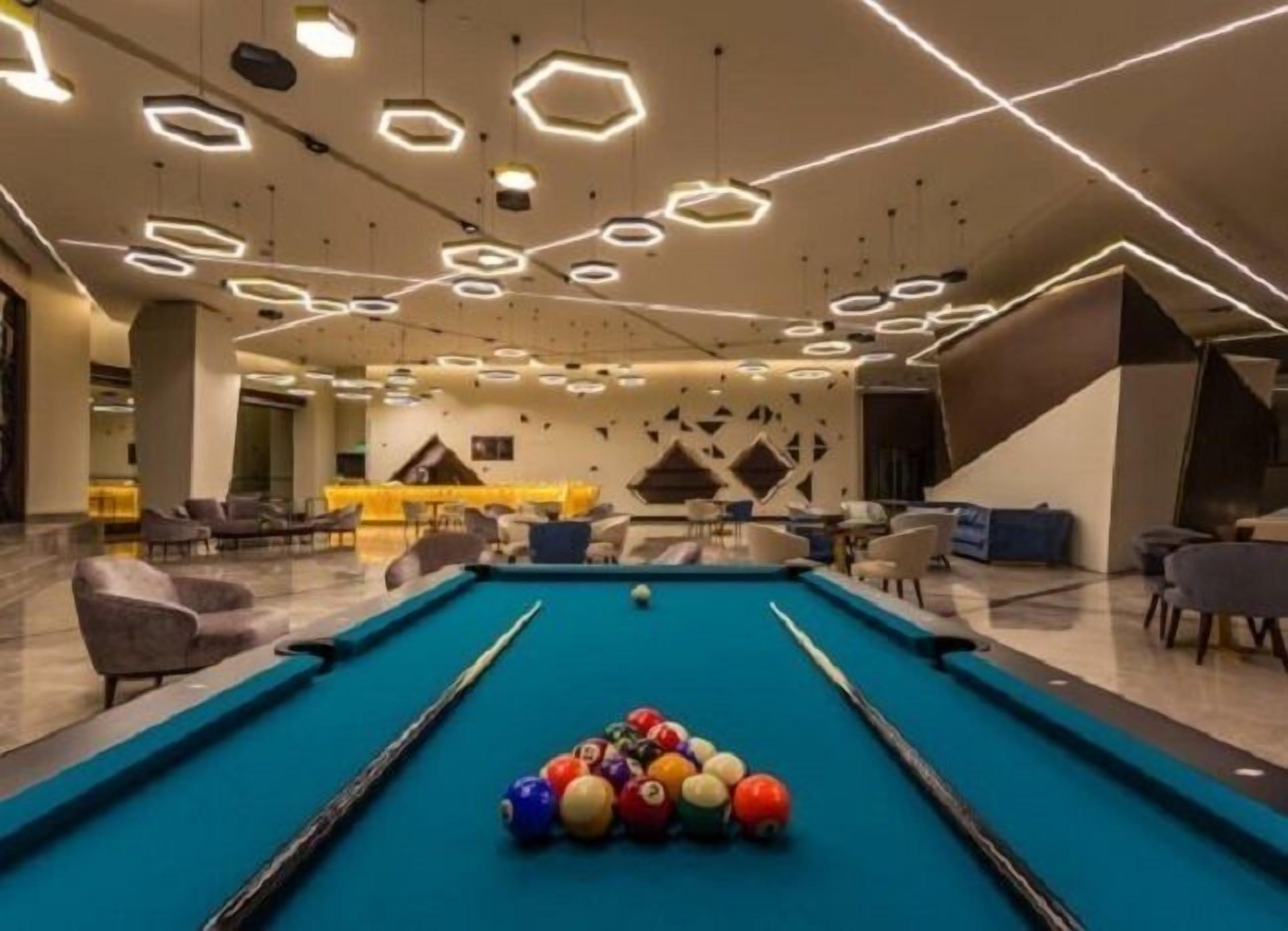 A pool table with balls, surrounded by modern seating and a geometric ceiling design.