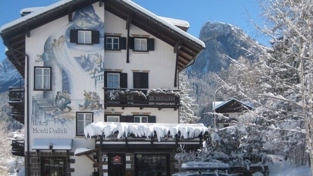 Een hotel met uitzicht op de bergen, een muurschildering van een besneeuwd landschap en een bordje met de tekst 'Hotel Monti Pallidi'.