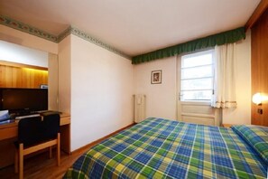 A room with a bed, a desk, a chair, a radiator, a window with curtains, and a picture on the wall.