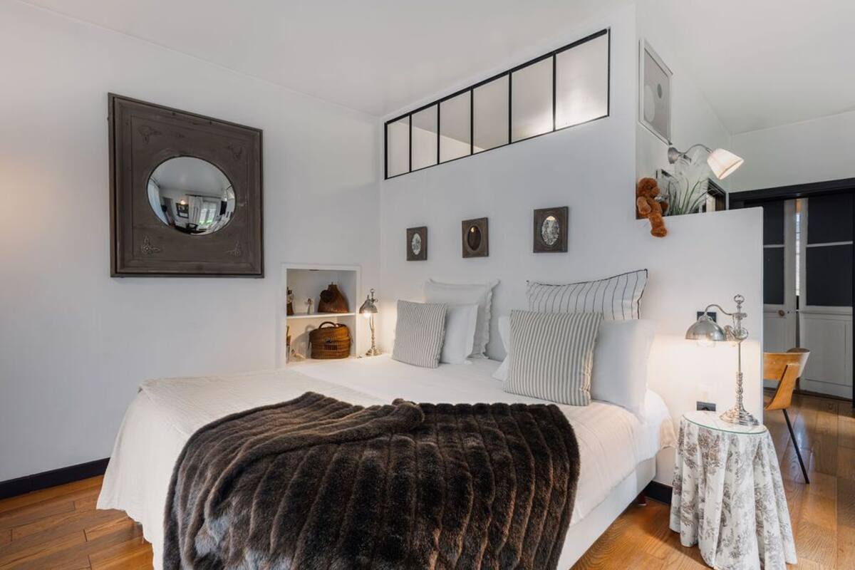 A modern bedroom with a large bed, a mirror, bedside tables, and a view of the outside.