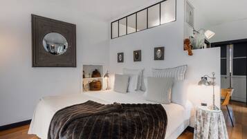 A modern bedroom with a large bed, a mirror, and a bedside table with a lamp.