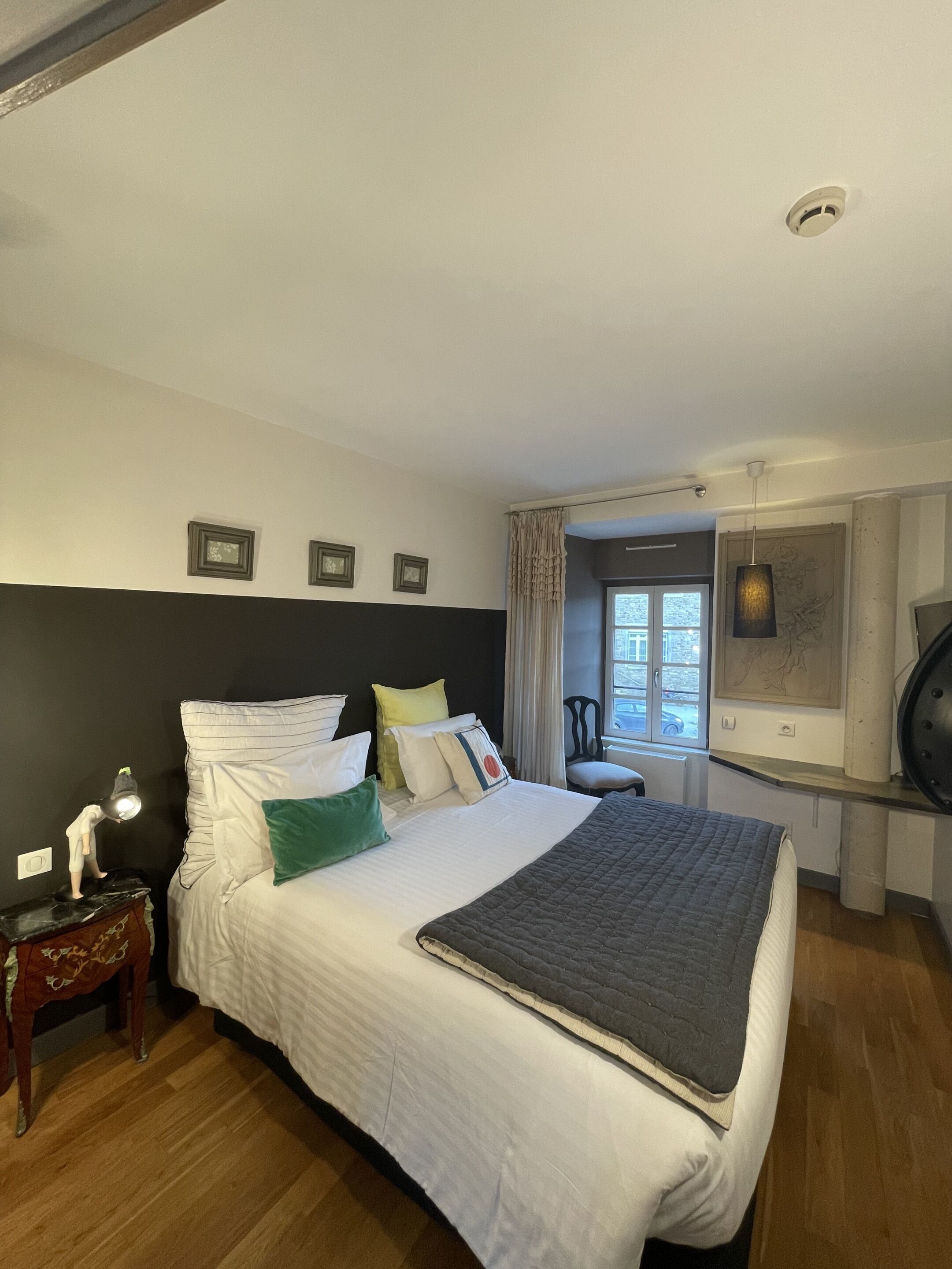 A neatly arranged bedroom with a bed, bedside table, lamp, and a window with curtains.