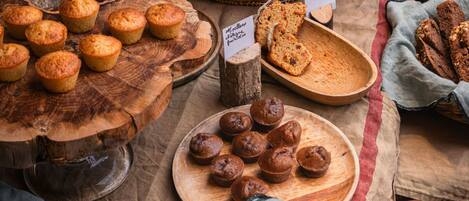 Variedad de productos horneados expuestos en tablas y cestas de madera, como muffins, croissants y pan, con etiquetas que indican los sabores.