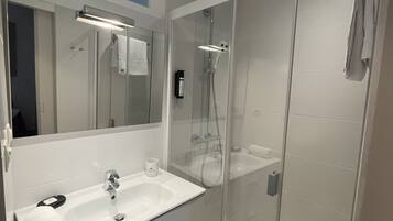 Un baño moderno con ducha envuelta en vidrio, un lavamanos blanco y un espejo grande.