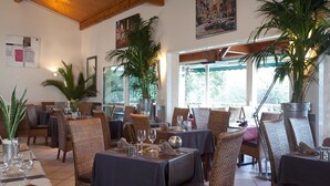 A restaurant with wicker chairs, tables set with wine glasses, and large potted plants. - Les Clos de Chaponost (Chaponost)