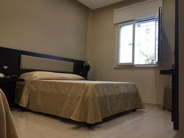 A bedroom with a bed, a nightstand, a window, and a radiator. - Grand Hotel Royal (Pompei)