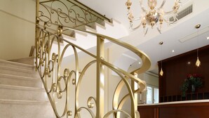 A grand staircase with ornate golden railings and a chandelier.
